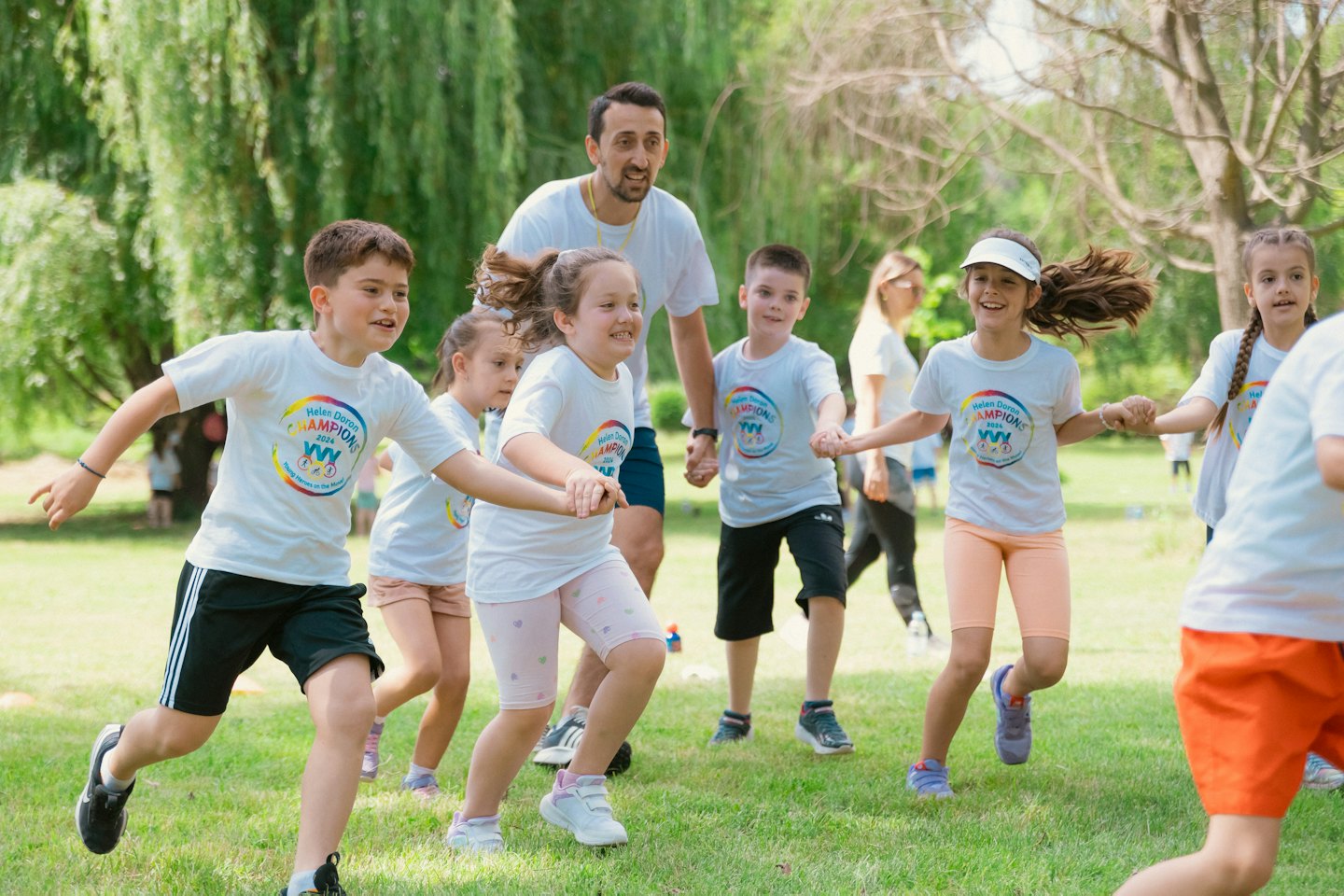 Ein Mann und Kinder in T-Shirts mit Markenlogo spielen im Park.